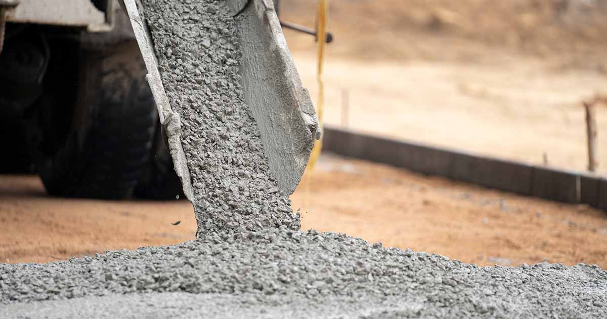 Concrete being poured on levelled dirt outside.