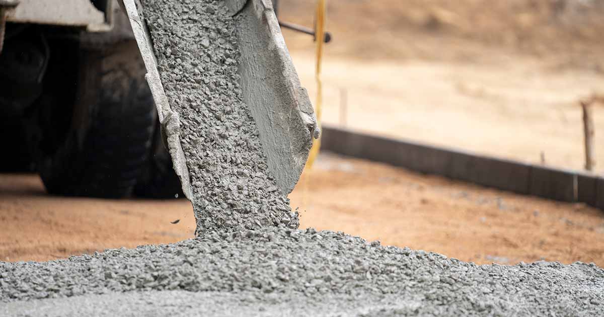 Concrete being poured on levelled dirt outside.