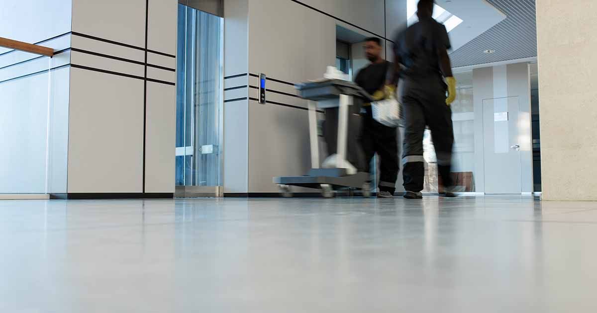 Two janitors walking in warehouse with polished concrete flooring.