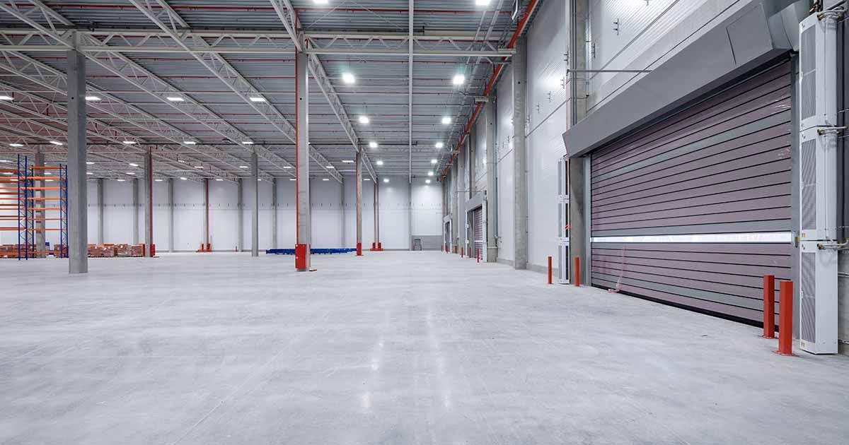 Polished concrete flooring in empty warehouse with large garage doors.