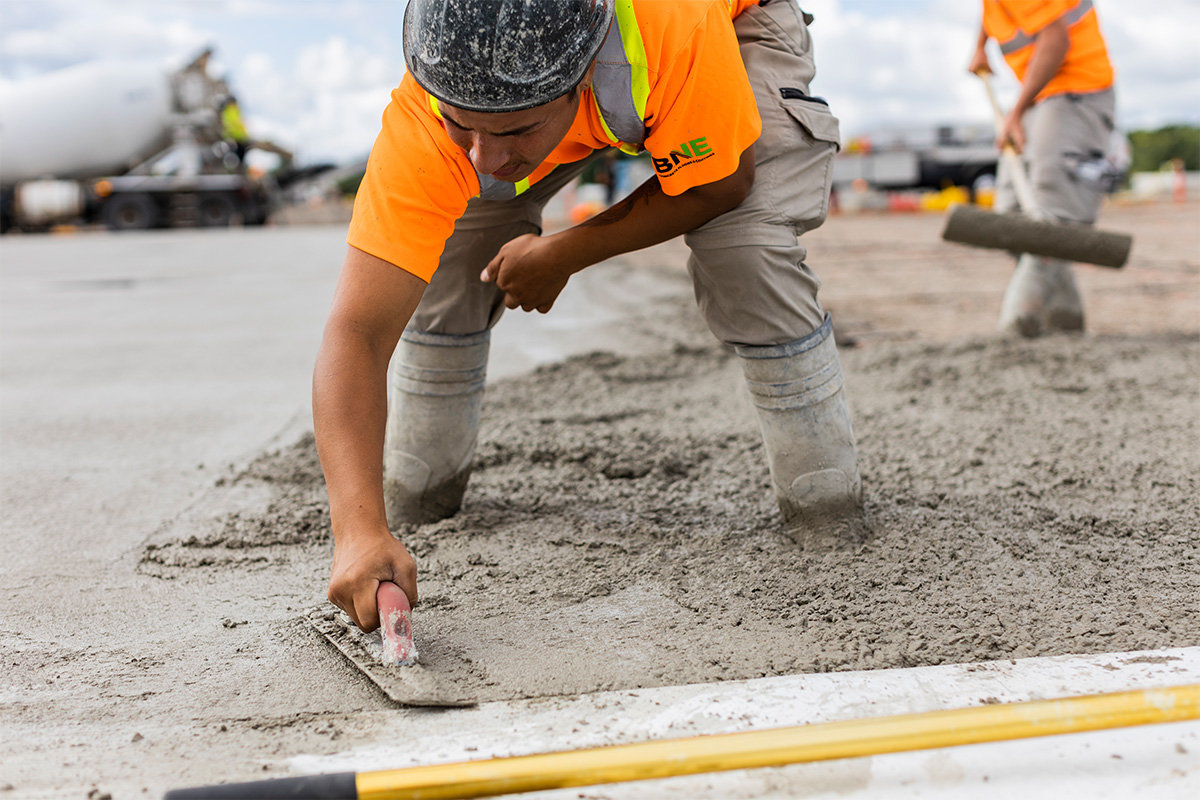 man in high-visibility vest smoothing concrete by hand